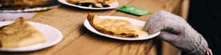 une main gantée attrape une assiette avec des crèpes par dessous la table