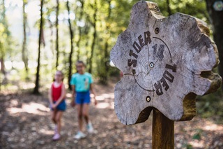 Un panneau originale en bois qui indique le Stoertoer. A l'arrière, deux petites filles se baladent dans la forêt. 