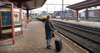 Une dame avec sa valise attend sur le quai le train qui entre en gare.